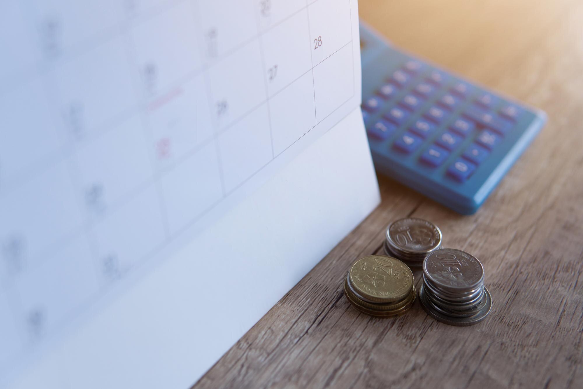 Kalender, kalkylator och mynt som illustrerar förfallodatum och betalningsplan
