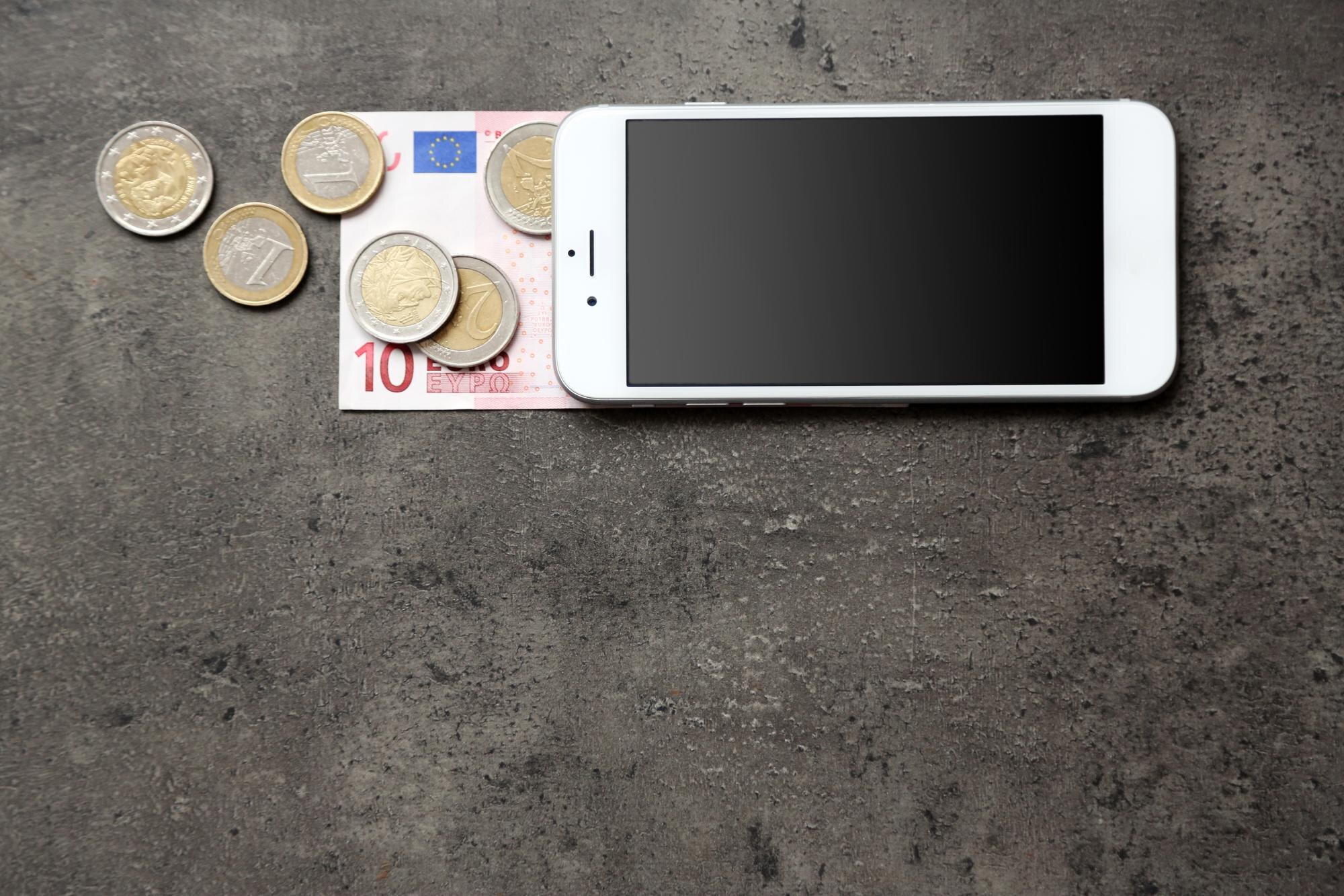 Smartphone med sedel och mynt som illustration av uttagsavgifter och valutakostnader