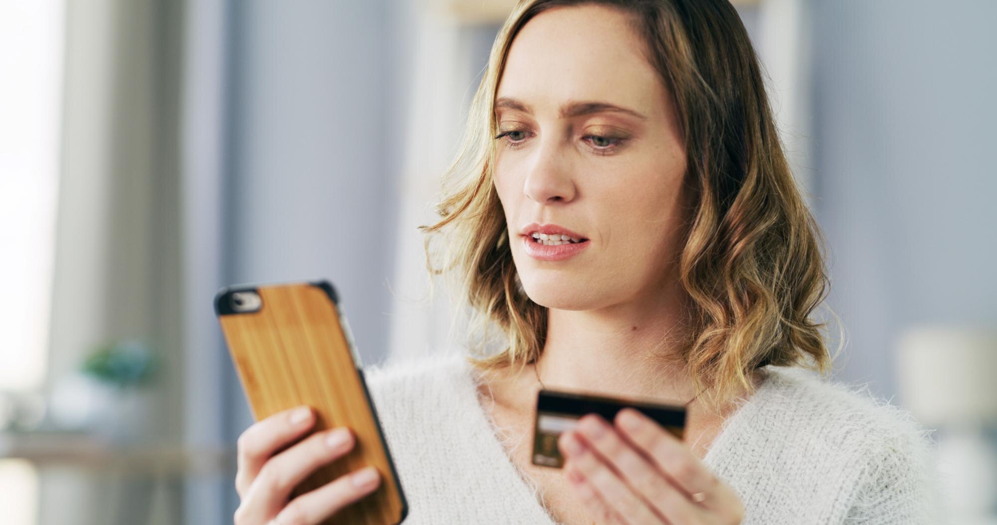 Kvinna som använder mobiltelefon och kreditkort, som illustration till ett kortuttag från casino som inte fungerar