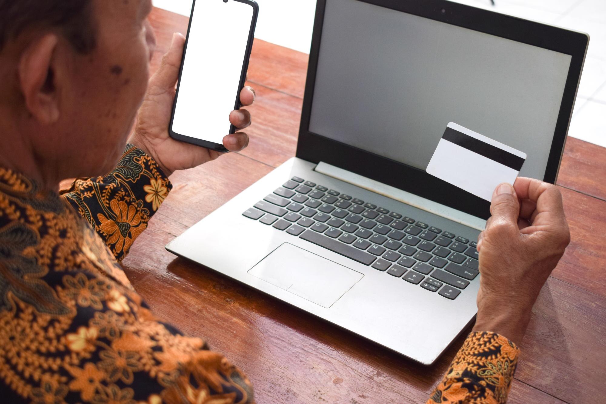 Person som genomför ekonomisk transaktion med kort, smartphone och laptop som illustration till automatiskt ändrad uttagsmetod