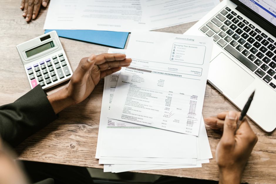 Person som går igenom finansiella dokument med kalkylator och dator inför en låneansökan