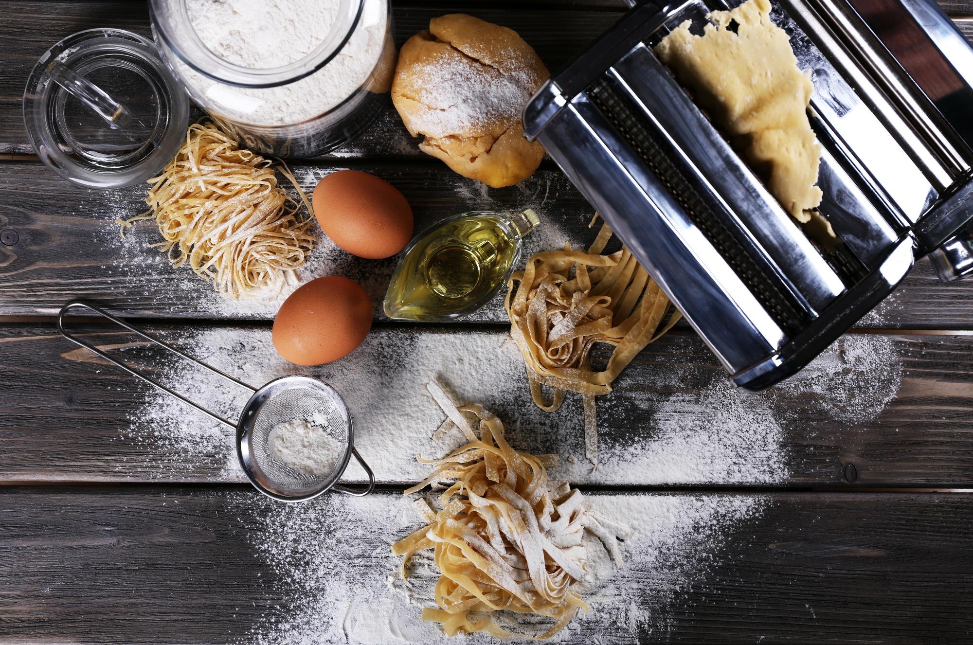 Pastamaskin och olika ingredienser för hemlagad pasta på träbord